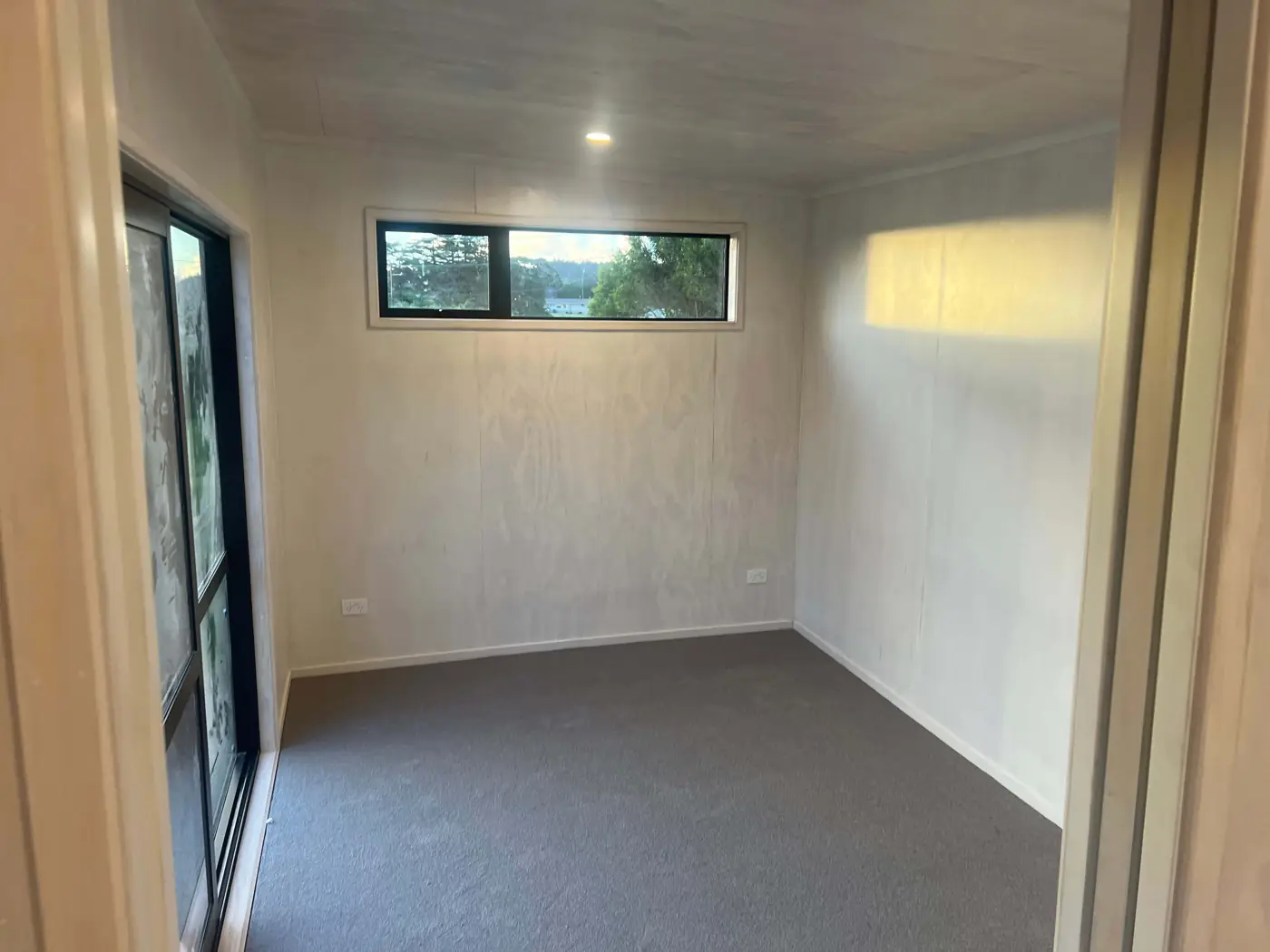 Carpeted bedroom with sliding door and high window in a Fab Living prefab home