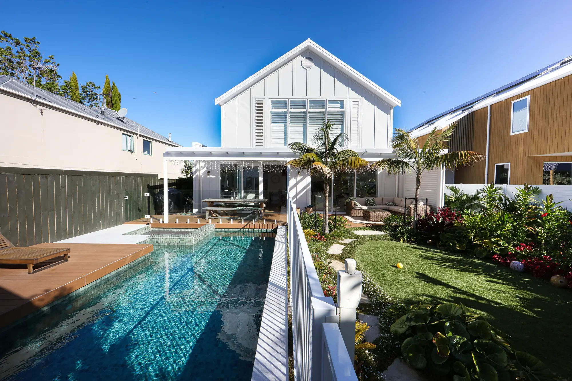 White gabled Auckland home with a pool, deck and tropical garden