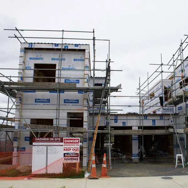 New Mangere homes wrapped and scaffolded during construction, with site safety signage at the gate