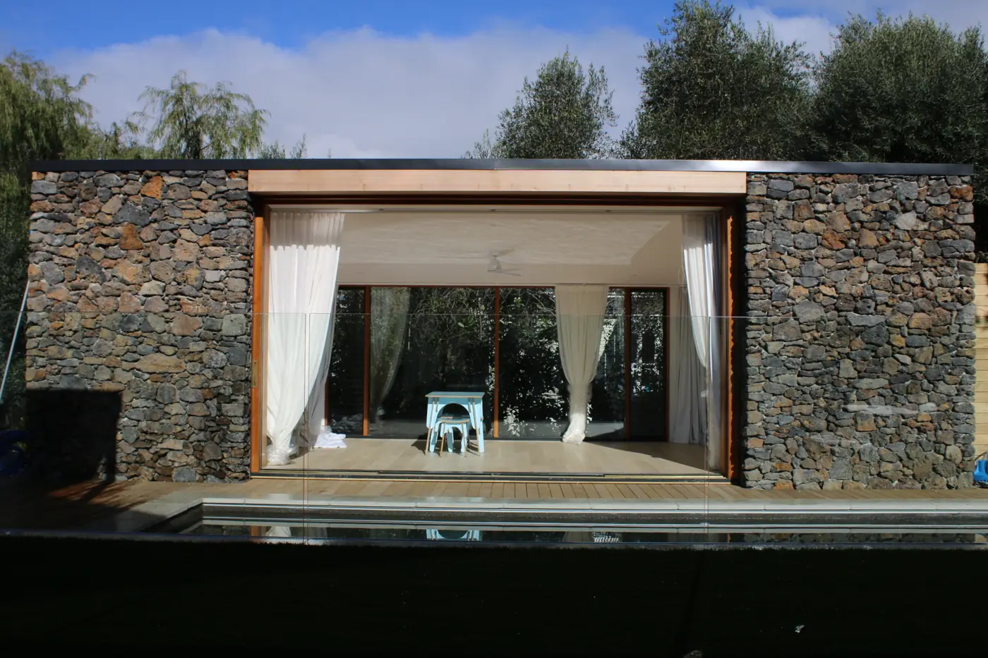 Stone pool house with timber decking beside the pool at a Mt Eden villa
